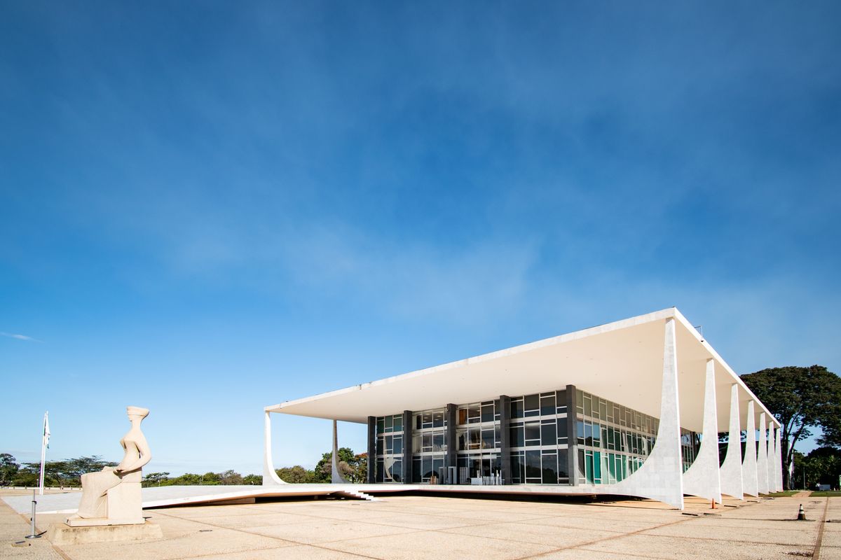 Fachada do Supremo Tribunal Federal em Brasília sob céu azul, com a escultura A Justiça à esquerda da entrada